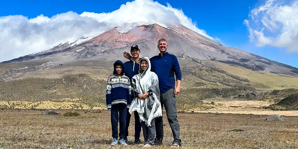 A family stands proudly beneath the cloud-covered glaciers of Cotopaxi Volcano in Cotopaxi National Park with kids