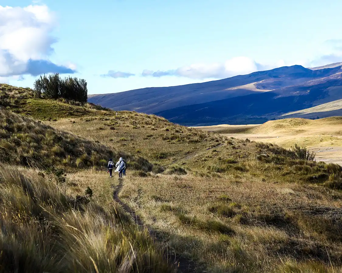 A family hikes through the rolling grasslands of Cotopaxi National Park toward a refuge