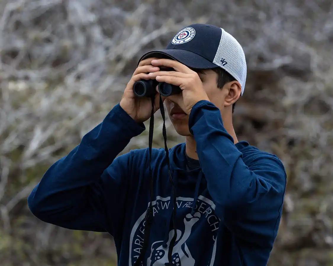 A teenager looks through binoculars while traveling in the Galapagos Islands