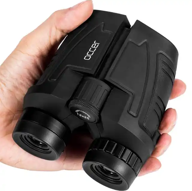 A hand holding a pair of Occer compact travel binoculars for adults and kids