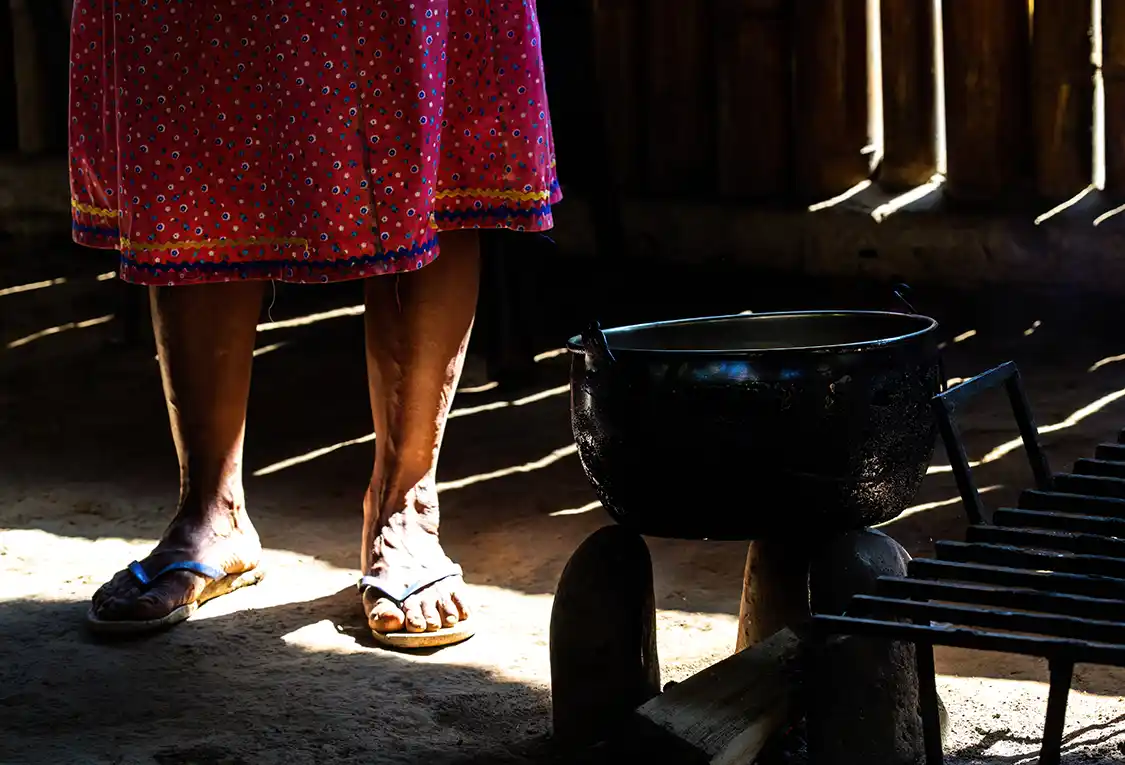 Sandaled feet of an Indigenous Pilche woman next to a pot over a fire