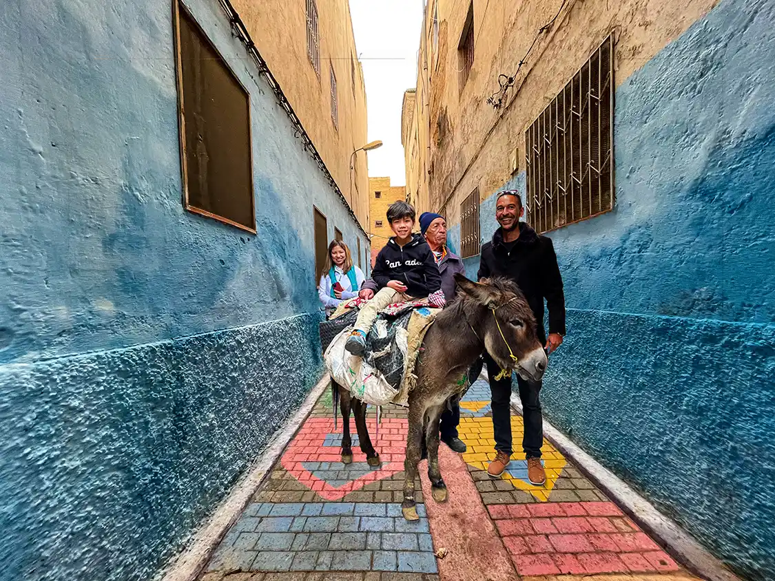 A boy sits on a donkey next to his mother while being guided through the streets of Fes Morocco
