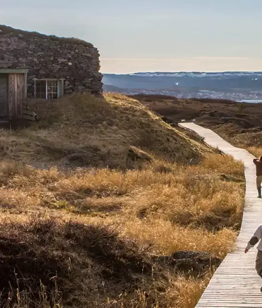 Two children walk along a stone walkway toward a stone buidling on the western coast of Newfoundland