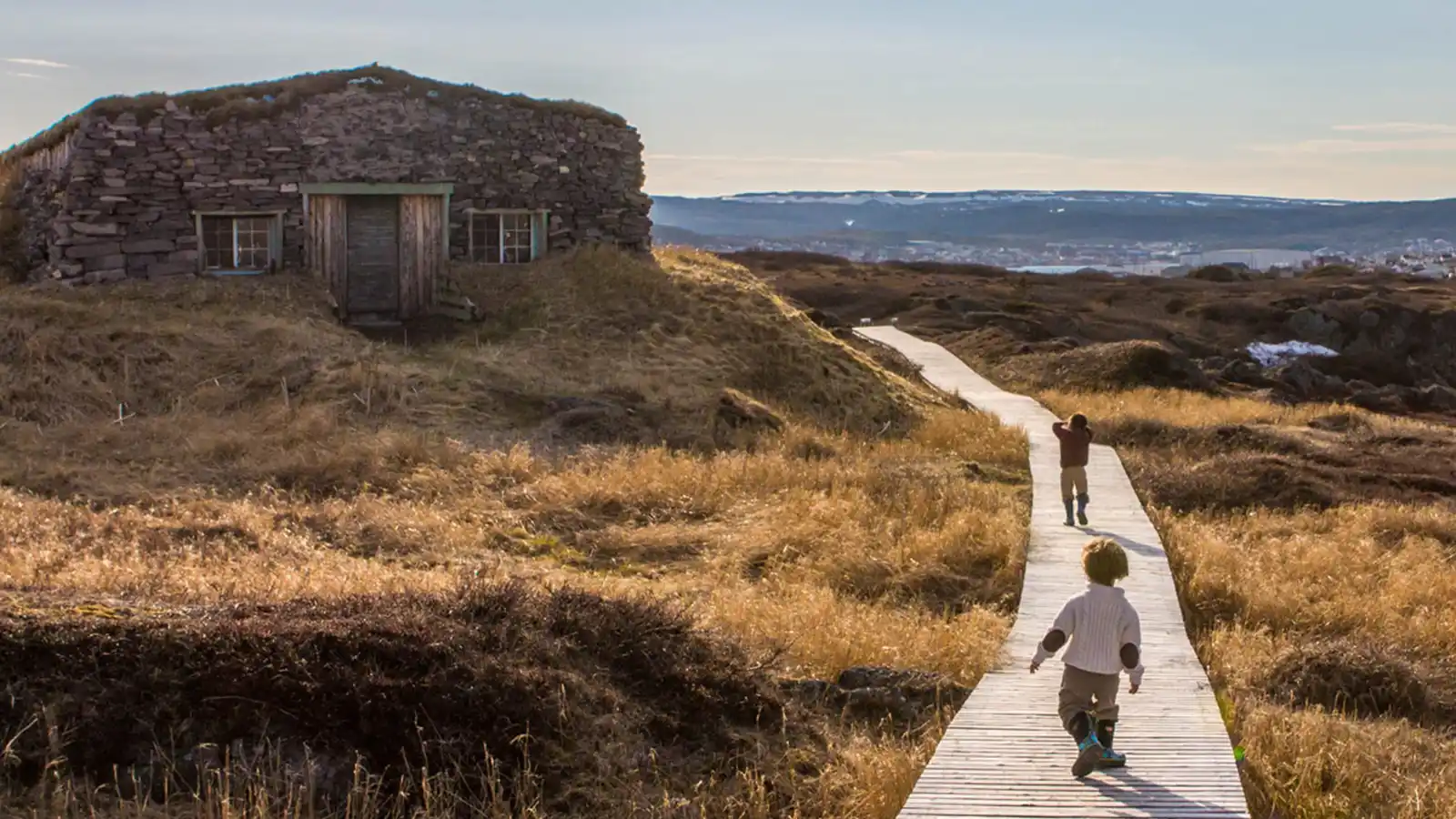 Two children walk along a stone walkway toward a stone buidling on the western coast of Newfoundland