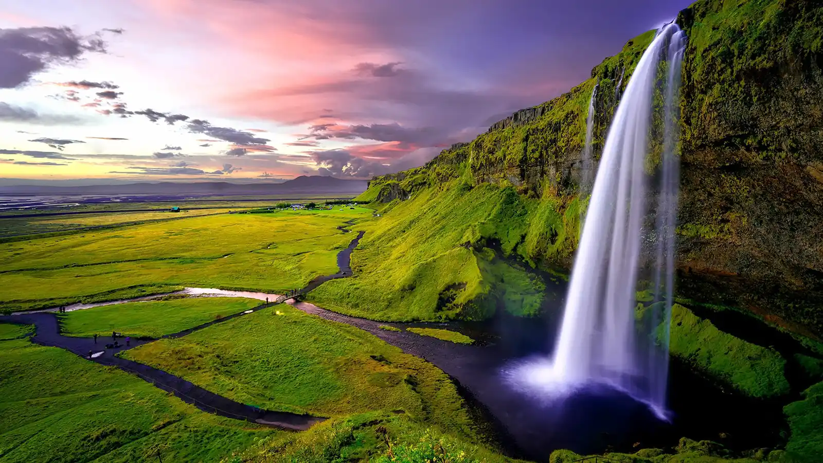 A waterfall pours from a cliff into a stream in an Iceland family travel guide