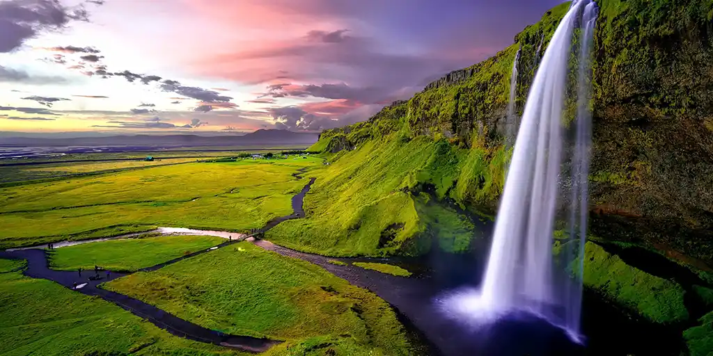 A waterfall pours from a cliff into a stream in an Iceland family travel guide