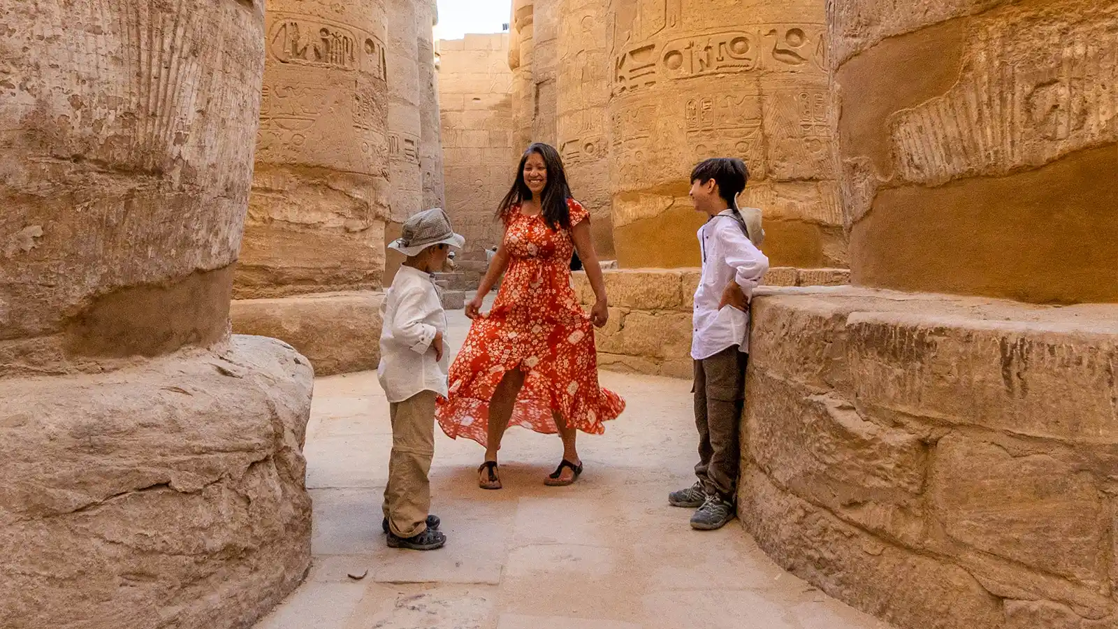 A woman dances through ruins in Luxor Egypt while her two boys watch excitedly