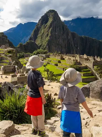 Two boys stand on an rock overlooking Machu Picchu, Peru during family travel