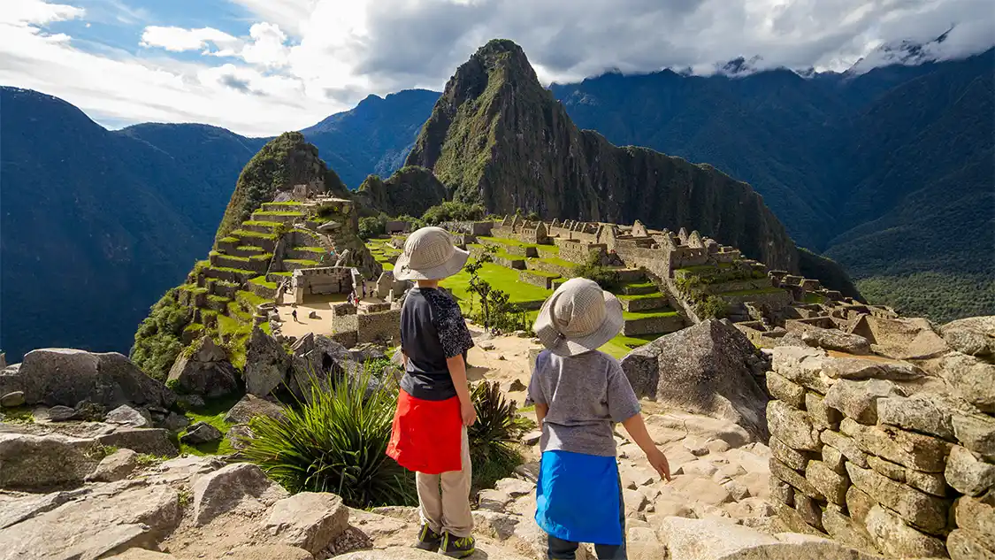 Two boys stand on an rock overlooking Machu Picchu, Peru during family travel