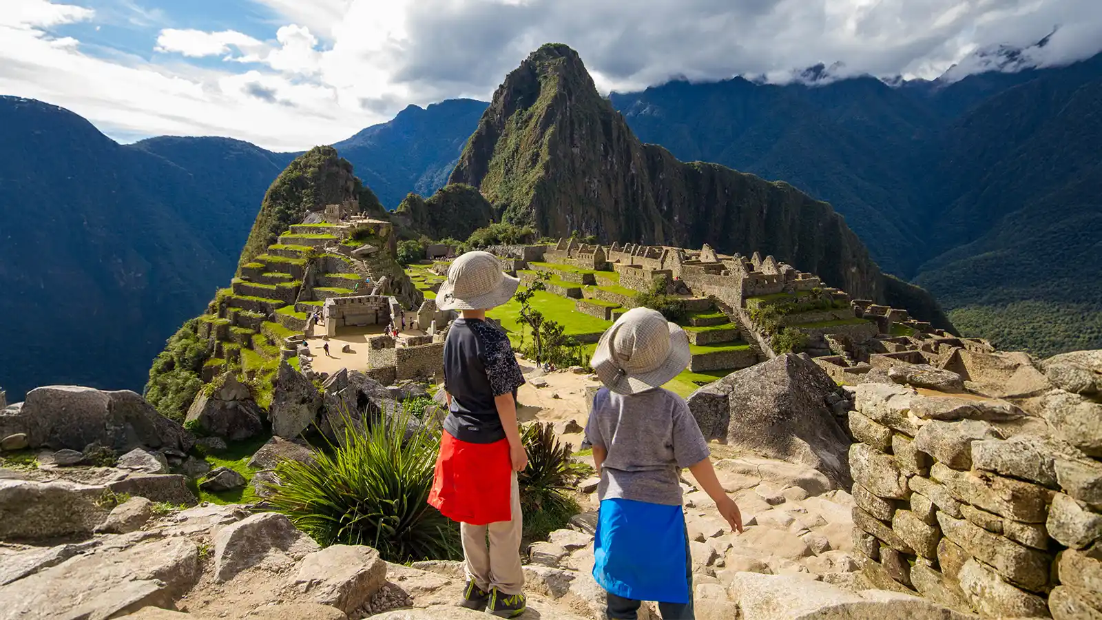 Two boys stand on an rock overlooking Machu Picchu, Peru during family travel