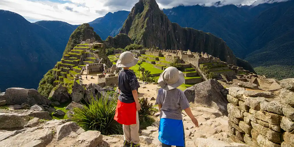 Two boys stand on an rock overlooking Machu Picchu, Peru during family travel