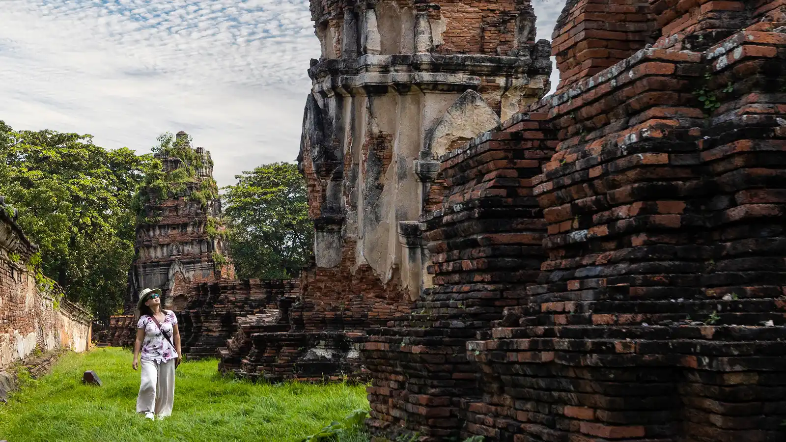 A woman walks through long green grass among temples in Thailand