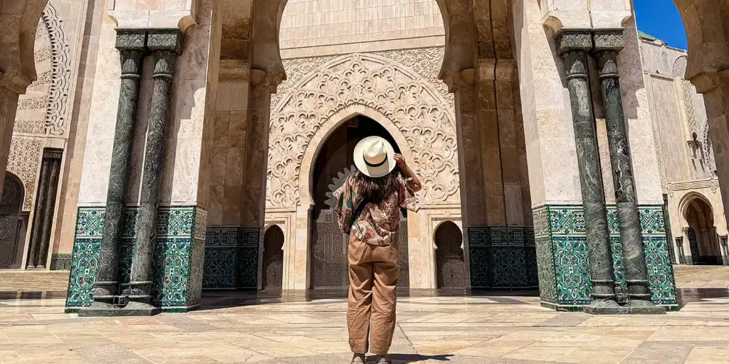 Woman holding a hat while looking up at a mosque in Casablanca,, Morocco