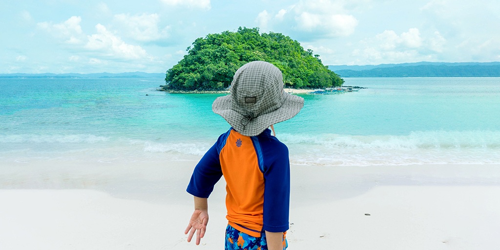 A young boy looks out at an island from a beach during family travel in the Philippines