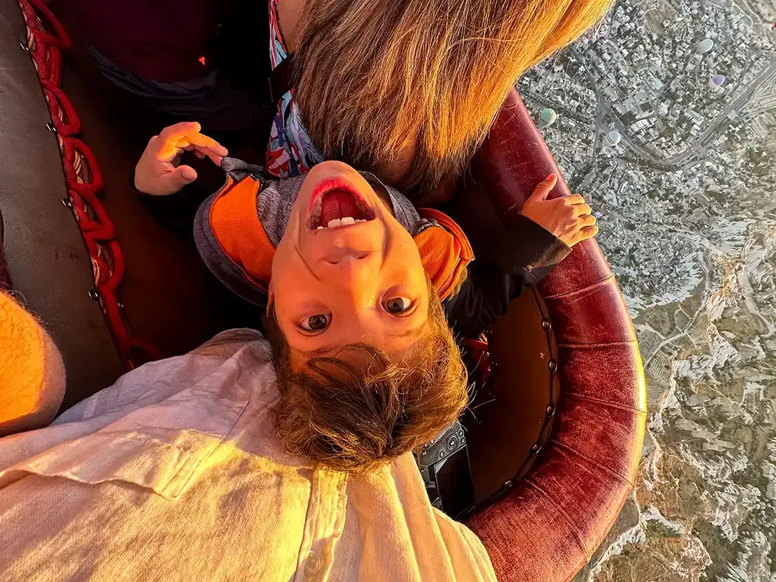 A boy looks up at a camera from a hot air balloon with a look of wonder on his face