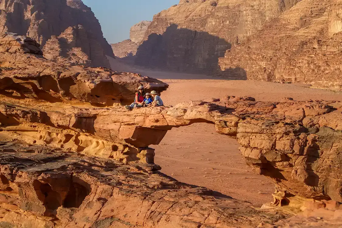 A family rests on a rock arch while hiking in Wadi Rum Jordan