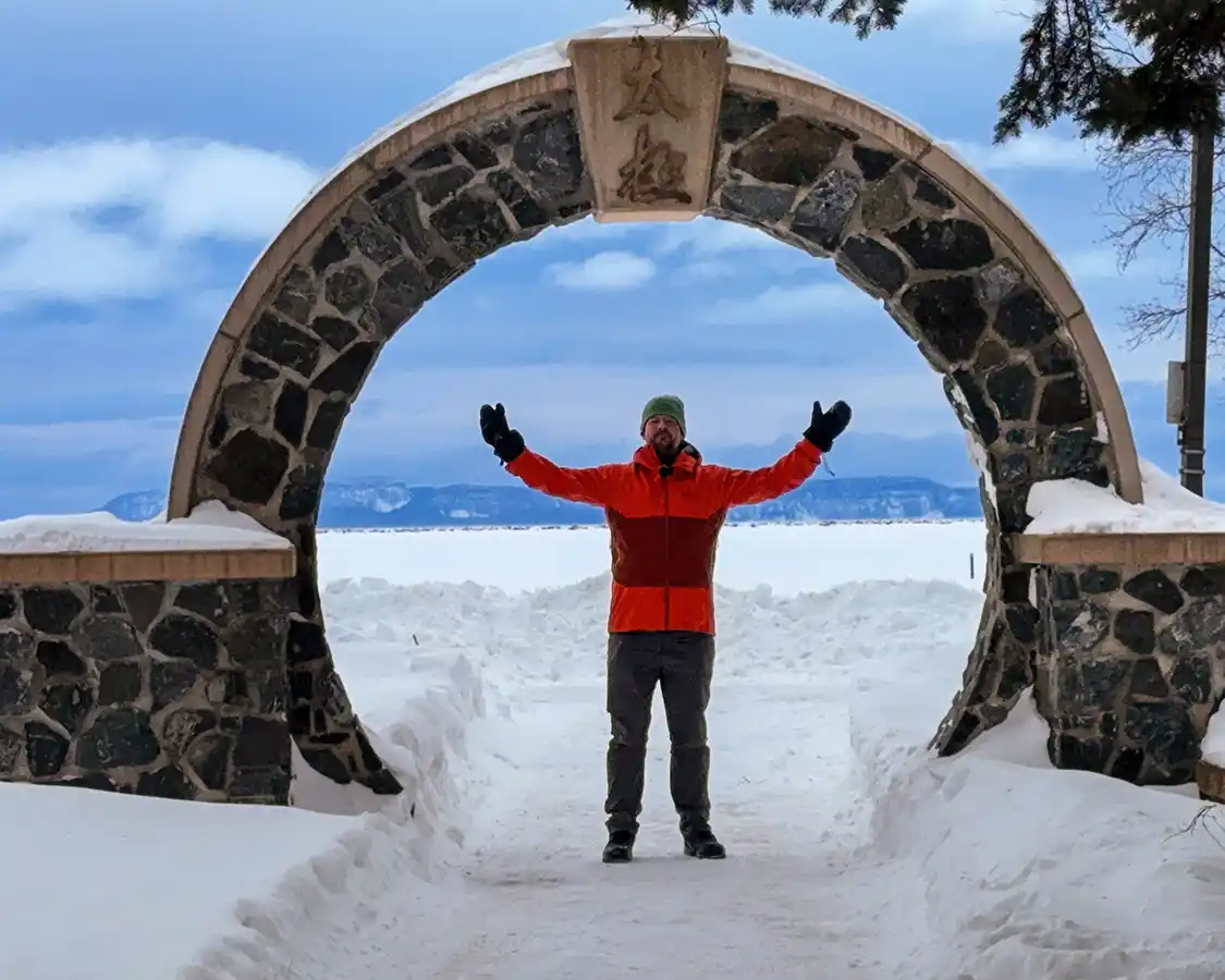 A man stands proudly framed by a moon gate on the Thunder bay Waterfront with Sleeping Giant in the background