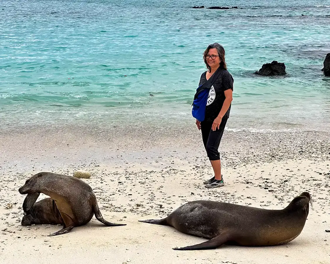 A woman stands next to a group of sea lions on a beach in the Galapagos Islands