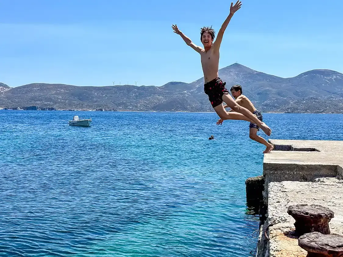 Two boys jump into the water in a small town in Milos Greece