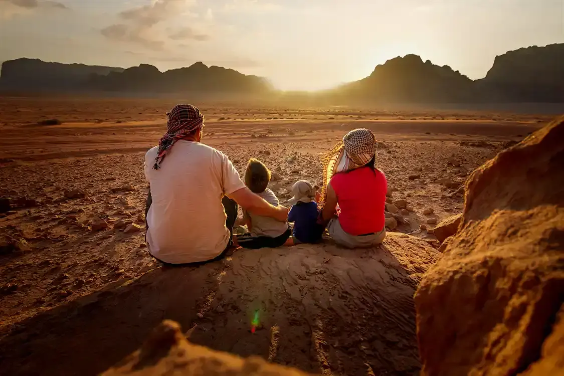 A family sits on a rock and watches the sunset in the Wadi Rum Desert in Jordan