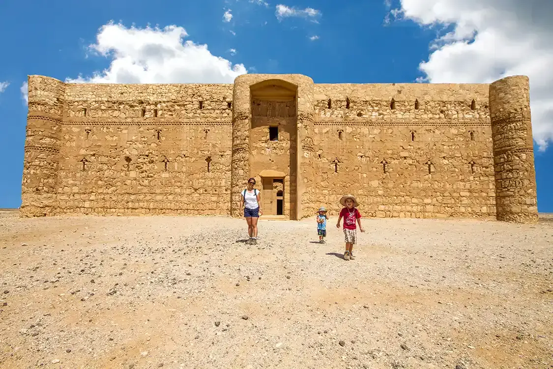 A woman and her children walk in front of a desert castle in Jordan