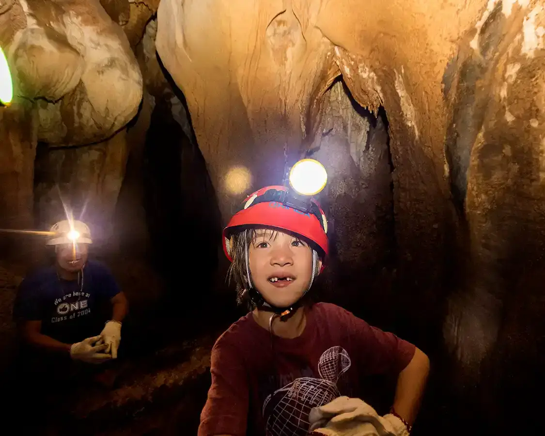 A young boy wearing a headlamp explores a cave in Palawan