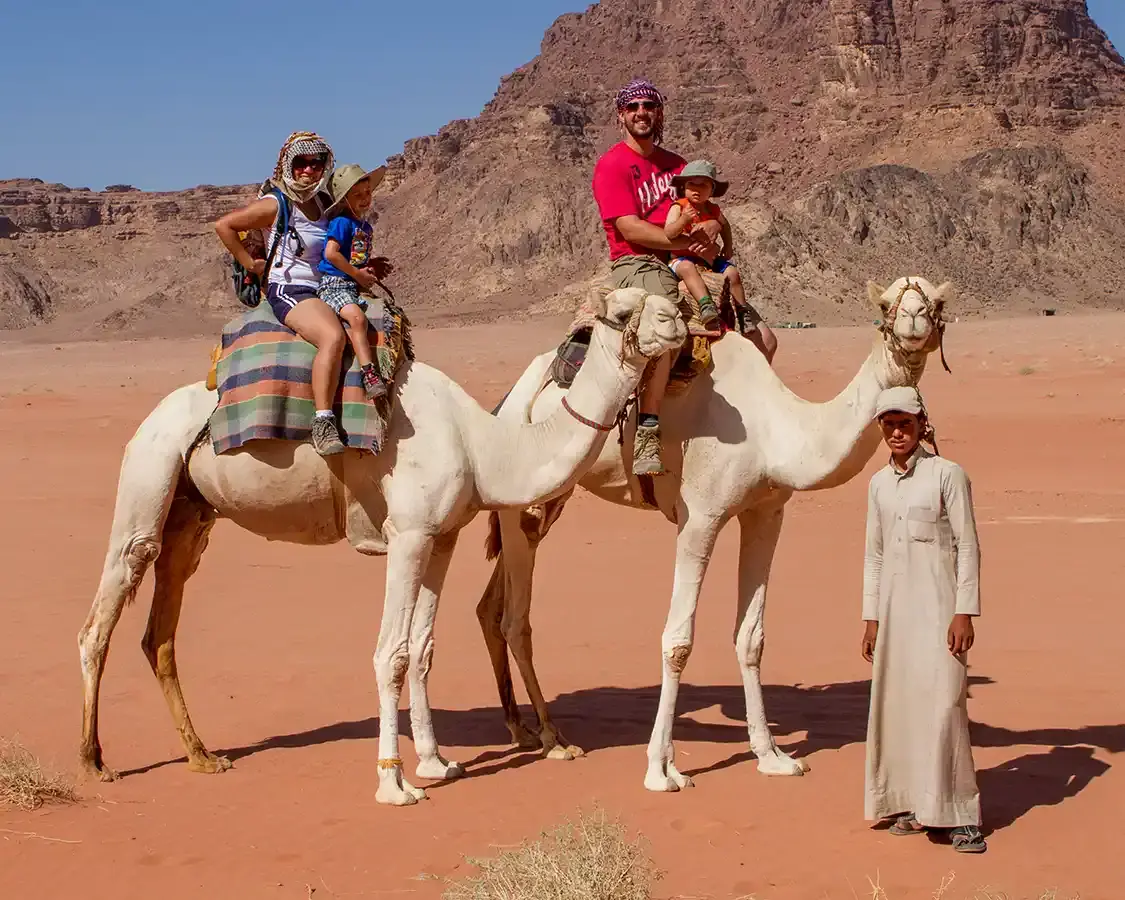 A young family rides camels through the Jordanian desert