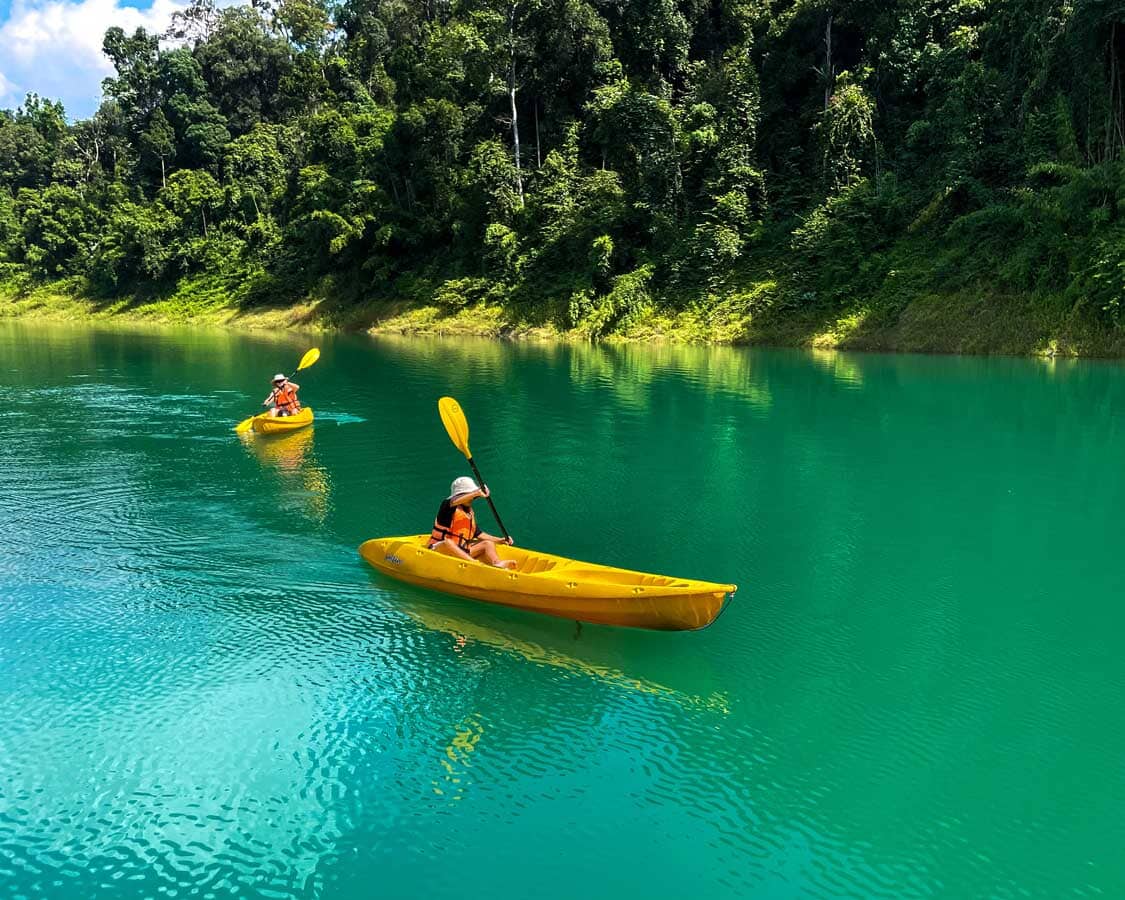 A family paddles through blue waters in Khao Sok National Park in Thailand