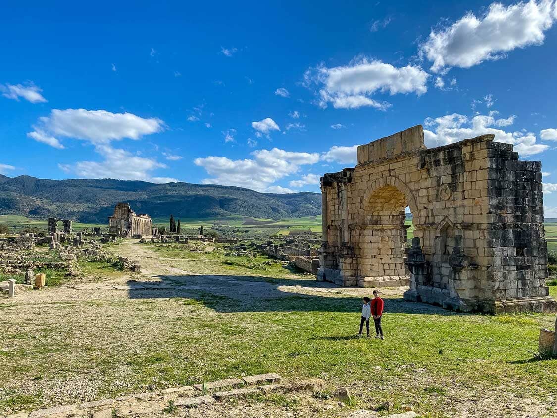 Two boys walk through the Triumphal Arch in Volubilis, Morocco