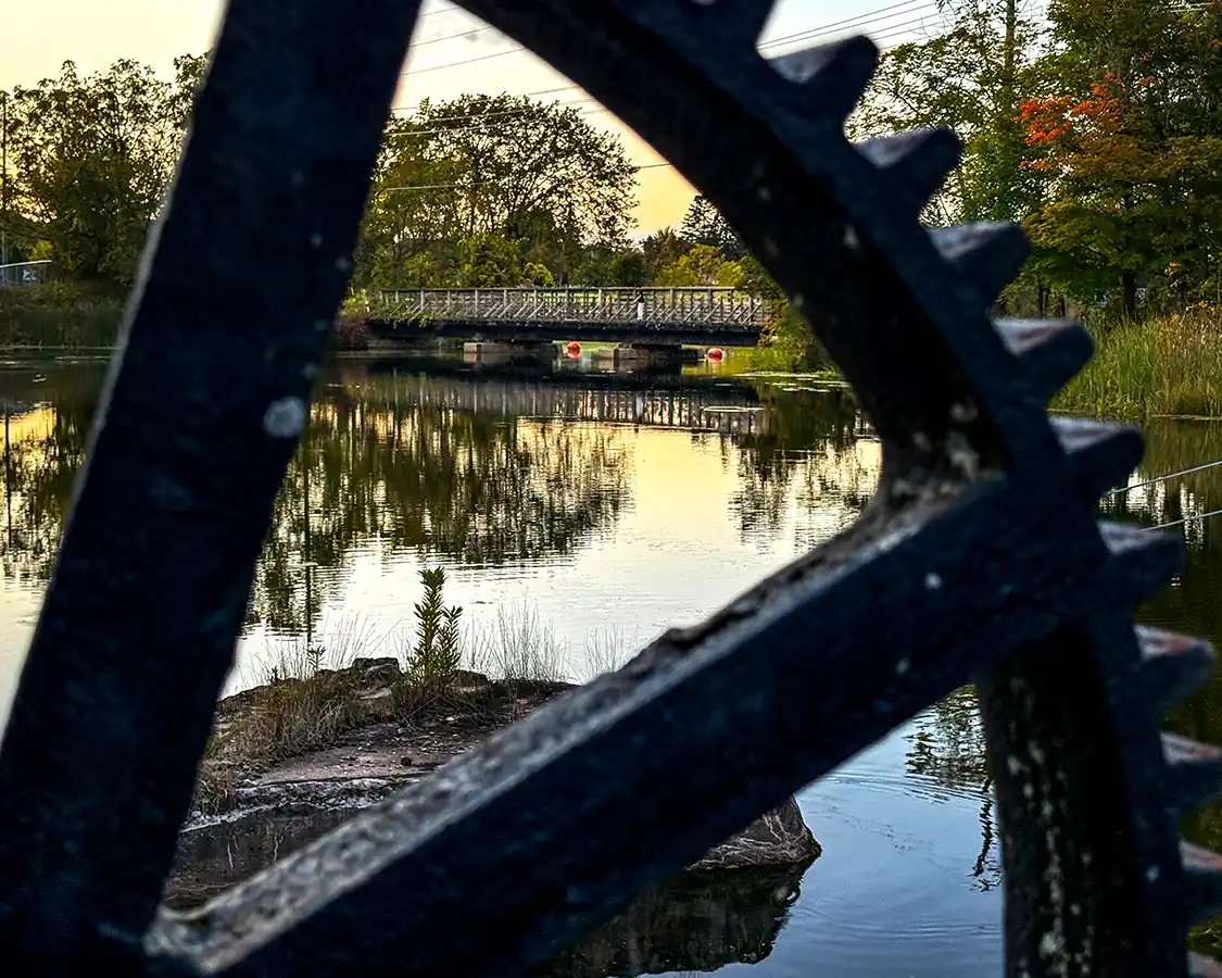 A Gananoque Trailway bridge crossing the Gananoque River seen through the spaces of a river dam gear